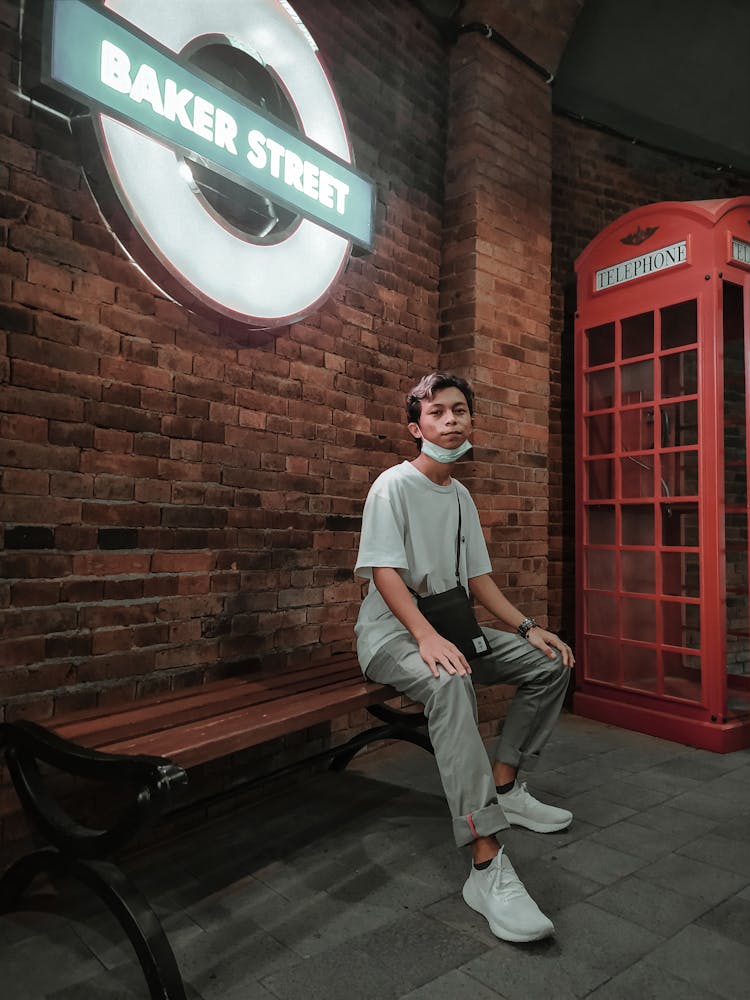 Stylish Young Ethnic Guy Resting On Bench Near Telephone Booth And Looking At Camera