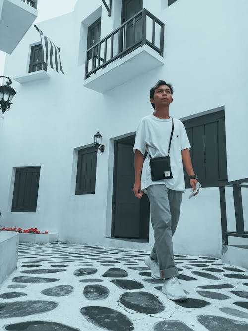 Full body of concentrated young ethnic male tourist in casual clothes exploring city while walking amidst traditional buildings during vacation