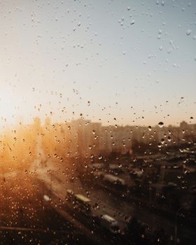 Sunlit raindrops on a window with Minsk cityscape in background, offering a serene view.