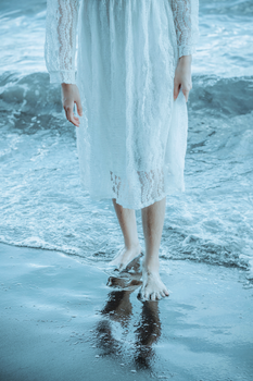 Crop anonymous barefoot female in white dress walking barefoot out of sea water on wet sandy shore