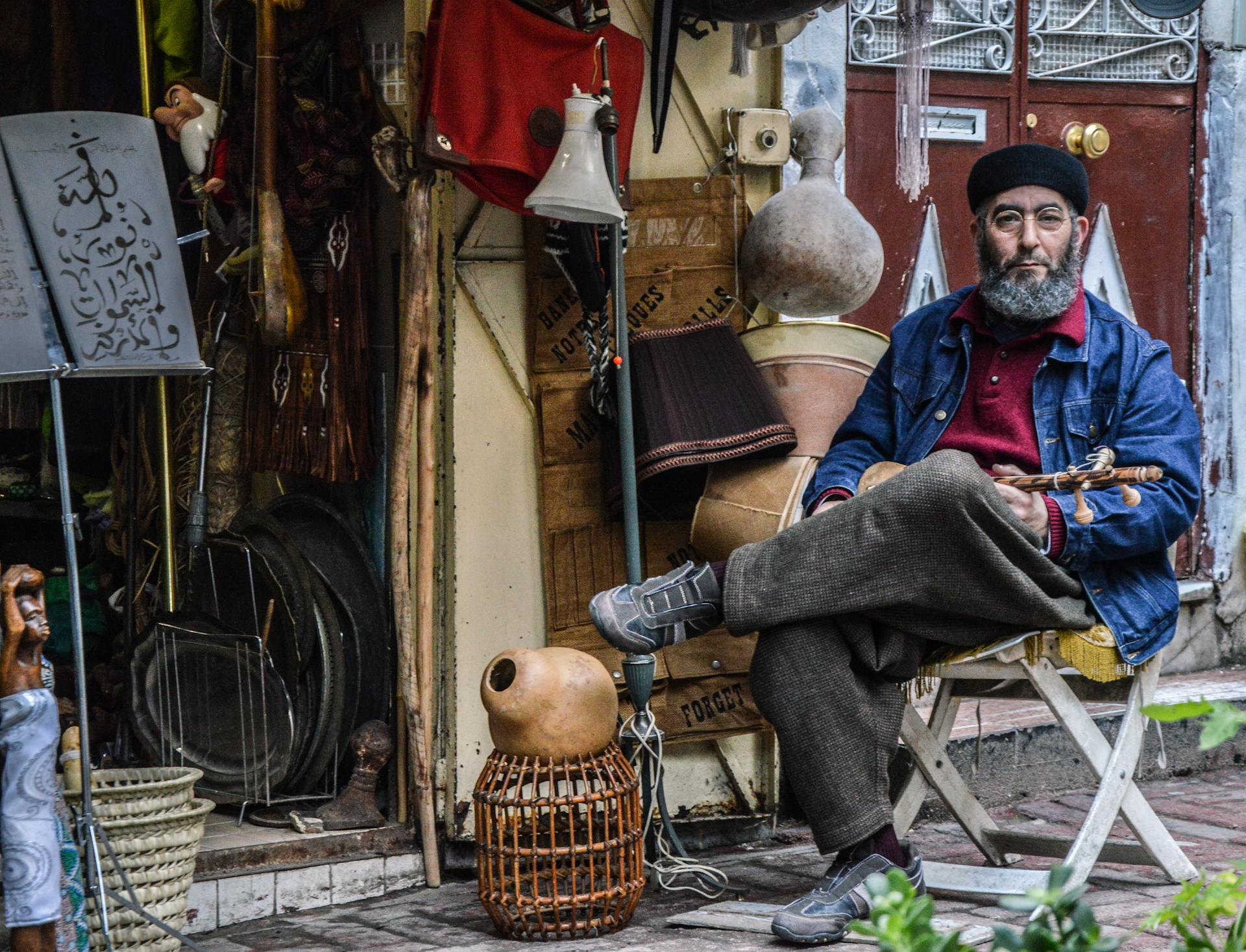 A traditional artisan sits amidst a collection of handcrafted goods in a Tangier market, showcasing Moroccan culture.