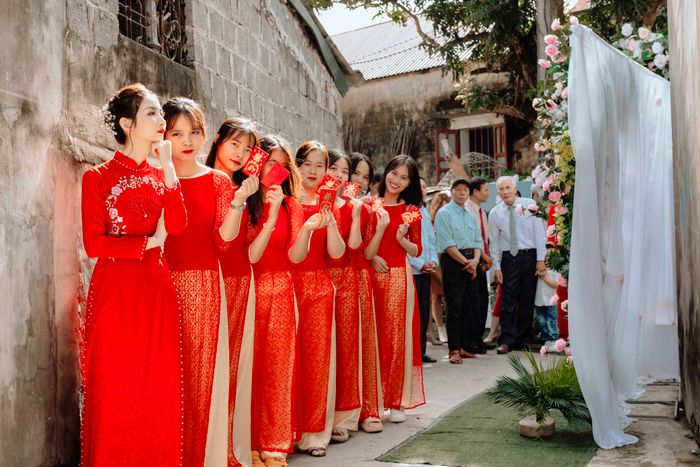 Dàn phù dâu áo dài đỏ cầm phong bao mừng cưới dưới cổng hoa