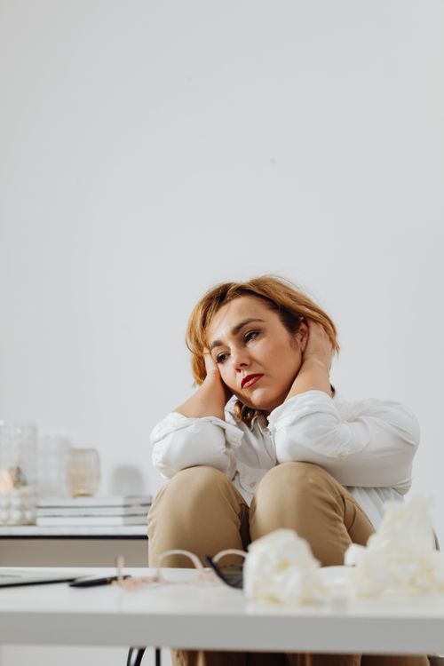 Free Thoughtful woman in white blouse sitting with brown pants, appearing pensive. Stock Photo