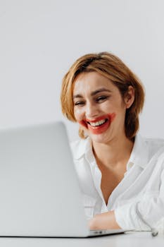 Laughing woman with red lipstick using laptop indoors.