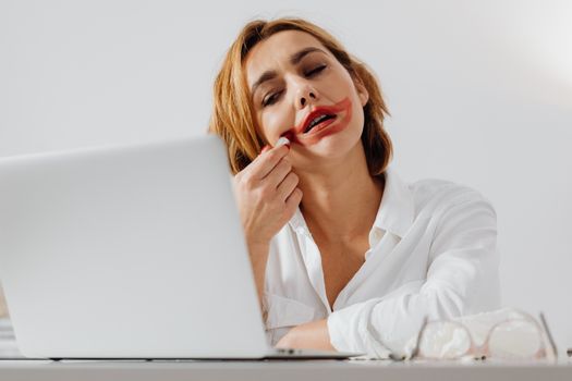 A woman with red lipstick smudged watching something on her laptop, indoors.
