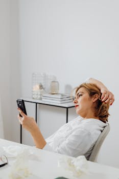 Woman lounging with a smartphone in a stylish indoor setting. Neutral tones and modern decor.