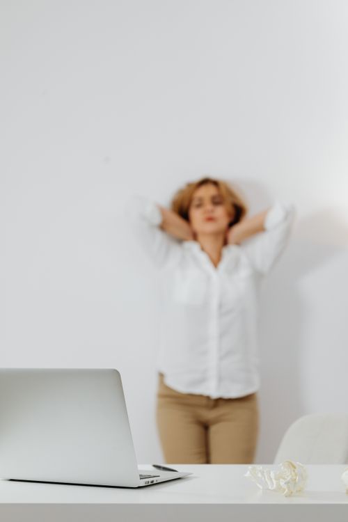 Free Woman standing relaxed behind a desk with laptop, in a minimalistic office setting. Stock Photo