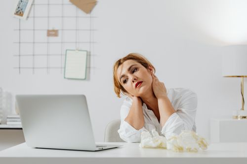 Free Tired woman sitting at desk with a laptop, appearing weary in a modern workspace. Stock Photo