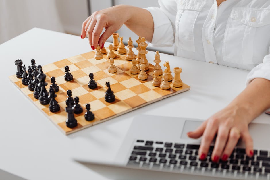 Close-up of a person playing chess and using a laptop indoors.