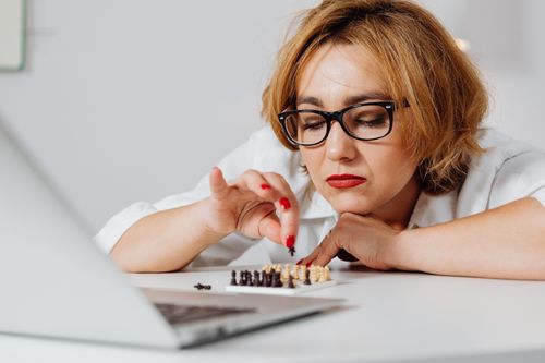 Free Focused woman with eyeglasses playing chess on a white table indoors. Stock Photo
