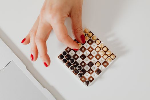 A hand with red nails moves a piece on a small chessboard, showcasing delicate strategy.