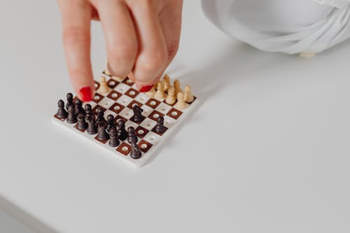 Person Playing a Mini Chess on White Surface