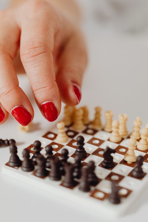 Free Hand with red nails playing miniature chess on a white surface, highlighting strategic gameplay. Stock Photo