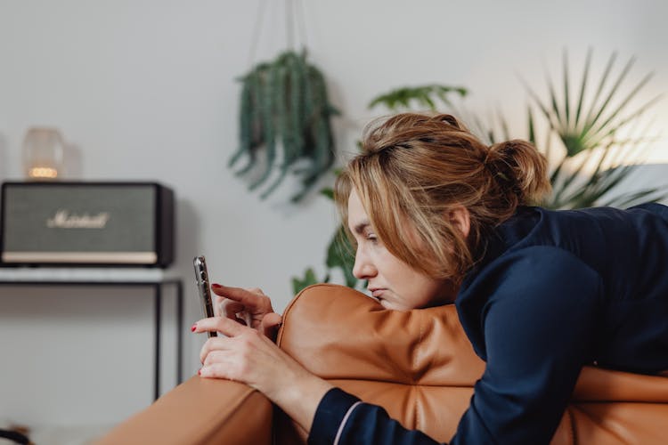 Woman With Messy Hair Lying Down On A Couch Using Her Cellphone