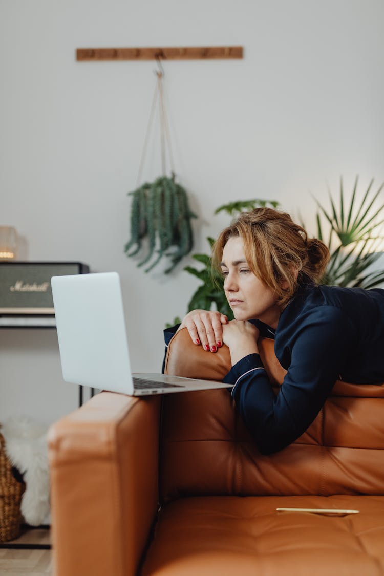 Woman On A Brown Leather Couch Staring At The Laptop