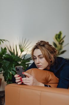 Woman lounging on a sofa using a smartphone amidst indoor plants, conveying a relaxed lifestyle.