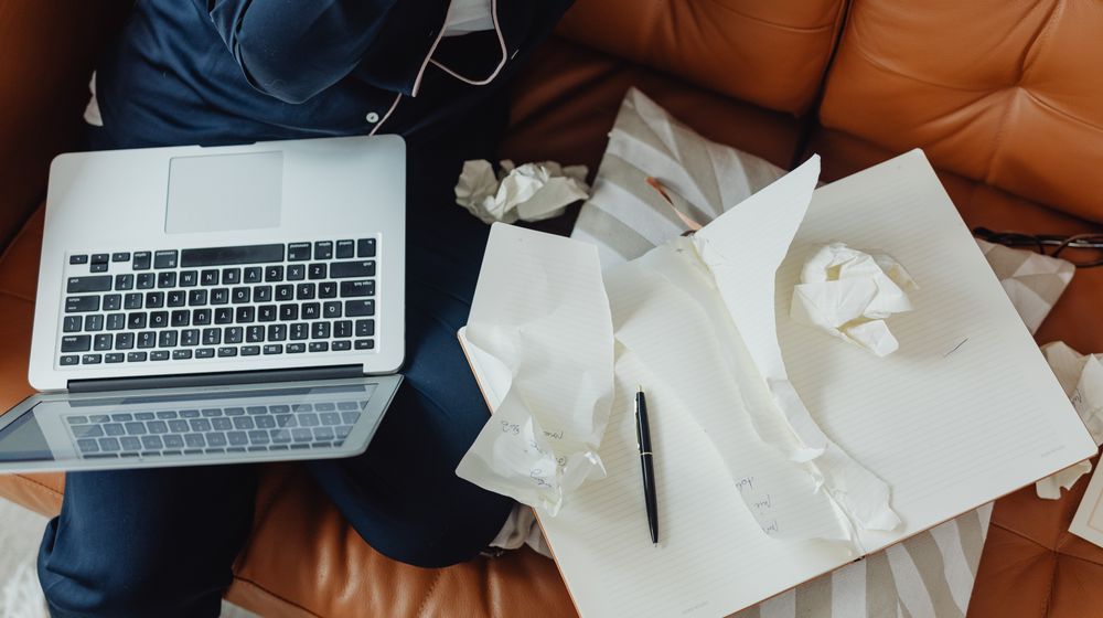A mess of crumpled papers, laptop, and notebook on a couch symbolizing creative chaos.