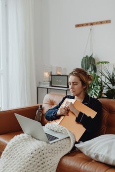 Woman relaxing on couch with laptop and coffee in cozy indoor setting.