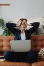 A Woman with a Headache Sitting on a Couch with Her Laptop