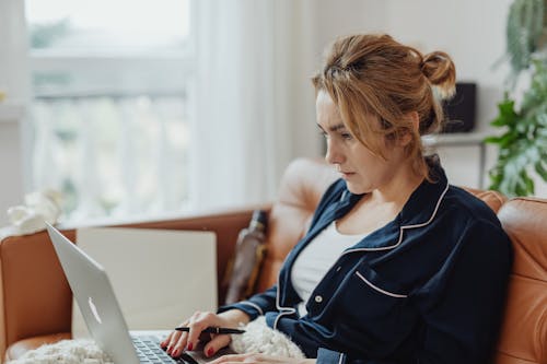 Free Woman Wearing a Pajama Holding a Pen and Laptop Stock Photo
