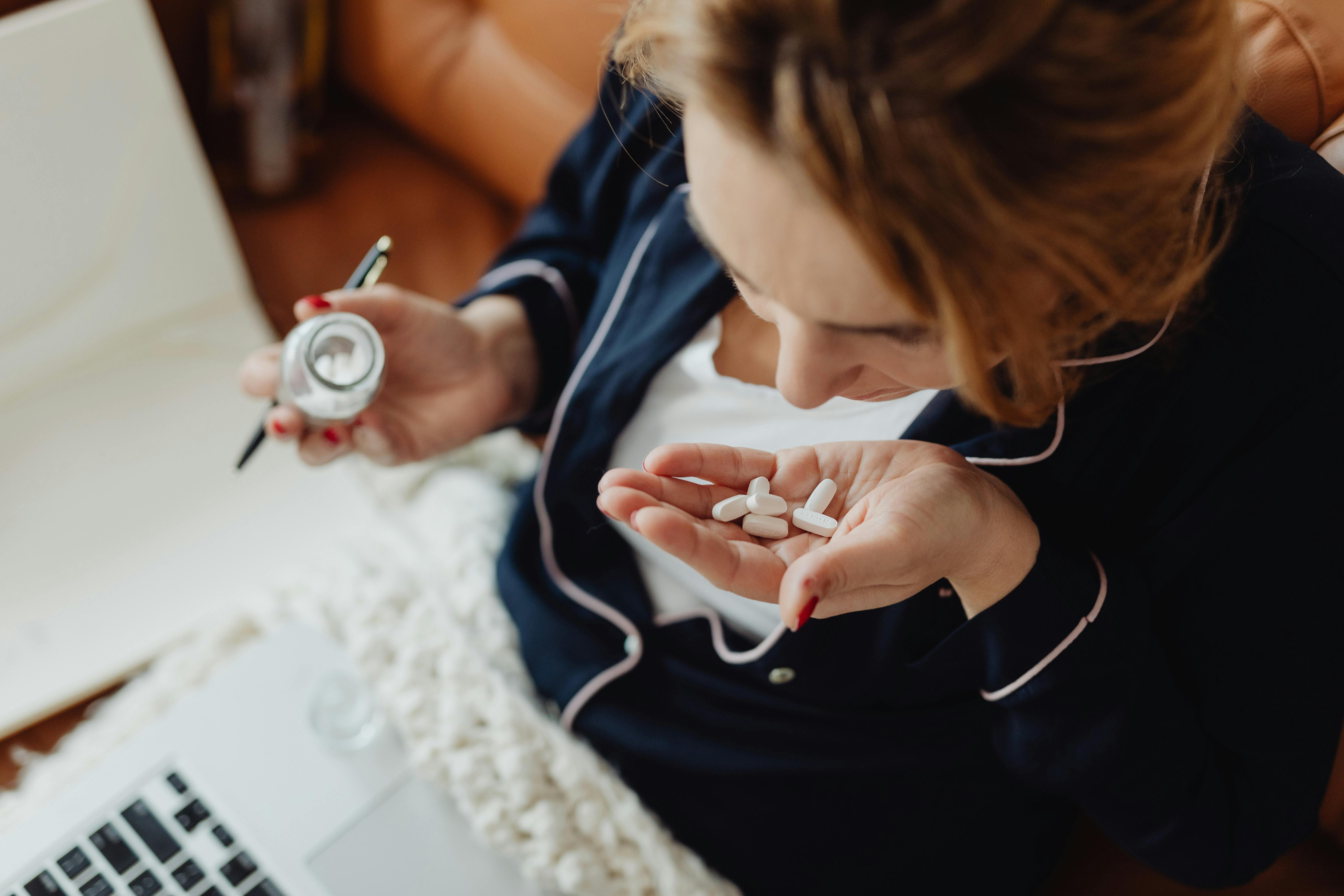 Free A woman in pajamas holding multiple pills, contemplating medication use. Stock Photo