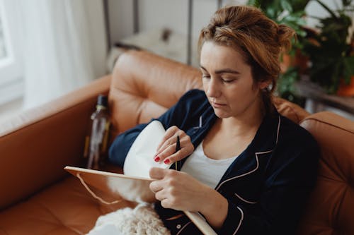 Free Woman Sitting on a Sofa While Writing on a Notebook Stock Photo