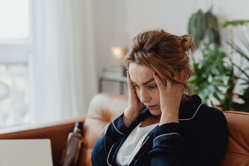 Free A woman in pajamas sits indoors with hands on head, showing stress and frustration. Perfect for mental health themes. Stock Photo