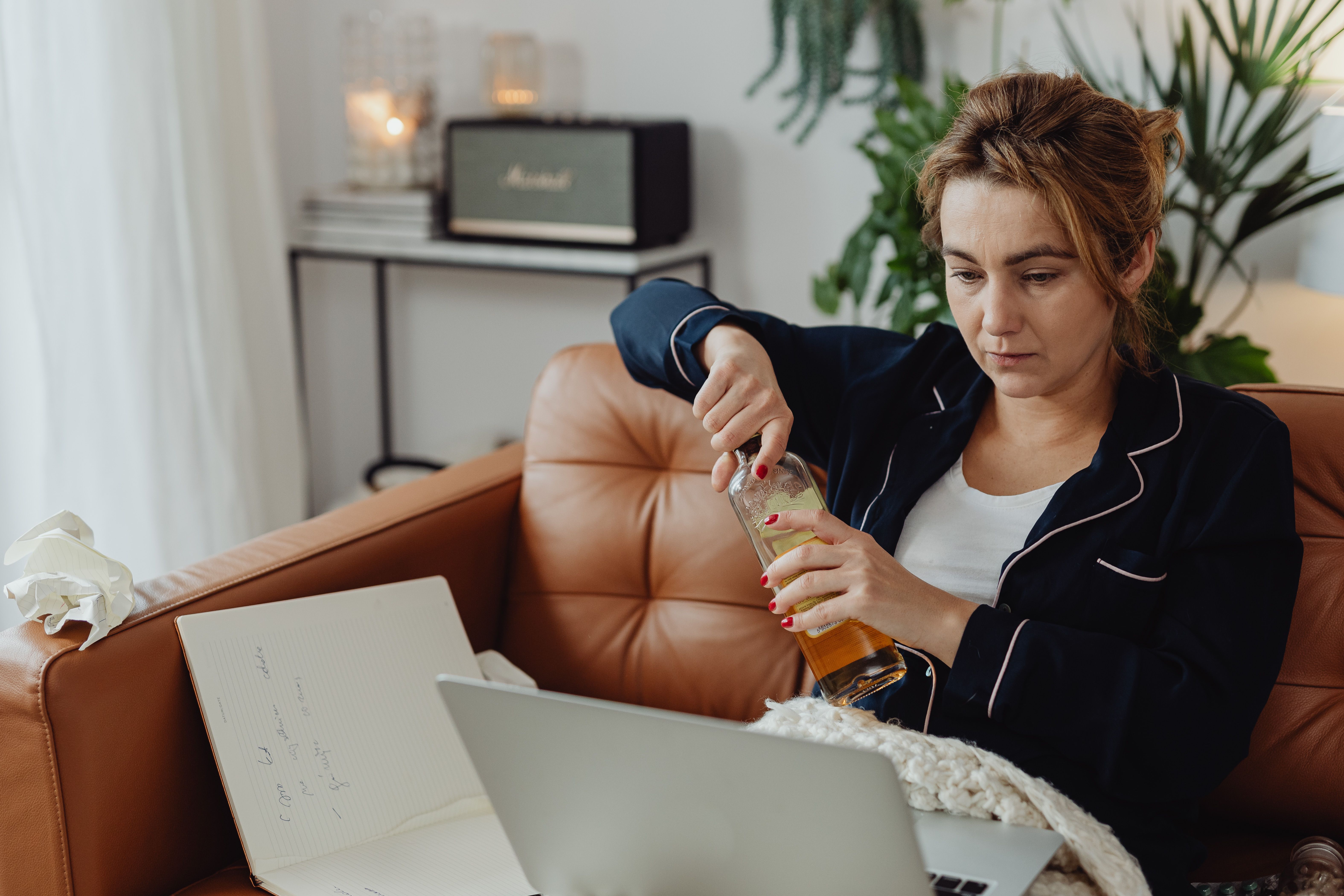 A person holding a bottle of liquor with a laptop on their lap