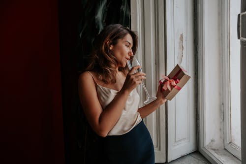 Young stylish woman enjoying champagne and looking at gift box