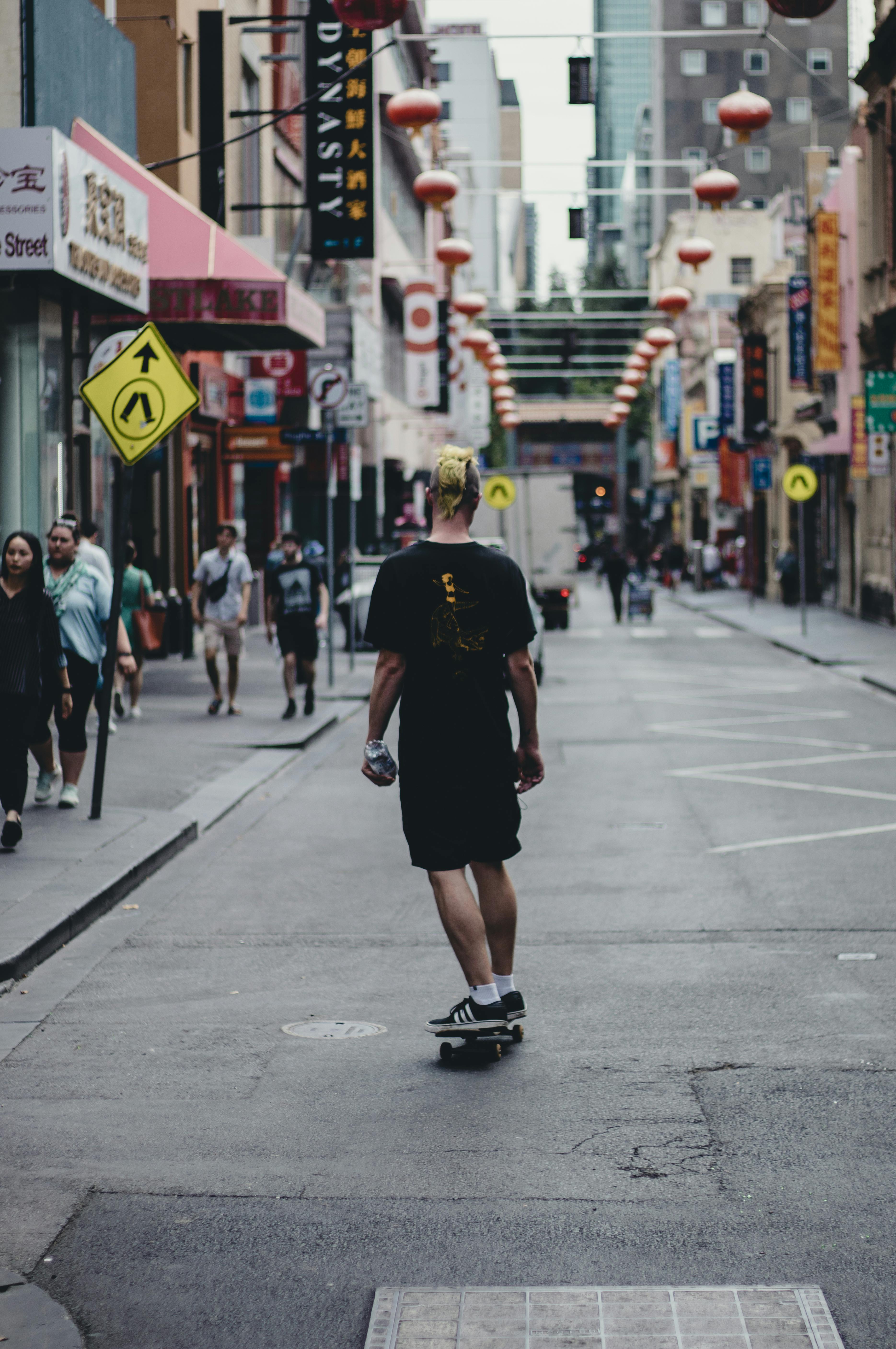 Free A skateboarder rides through a busy Chinatown street, surrounded by urban culture and vibrant architecture. Stock Photo