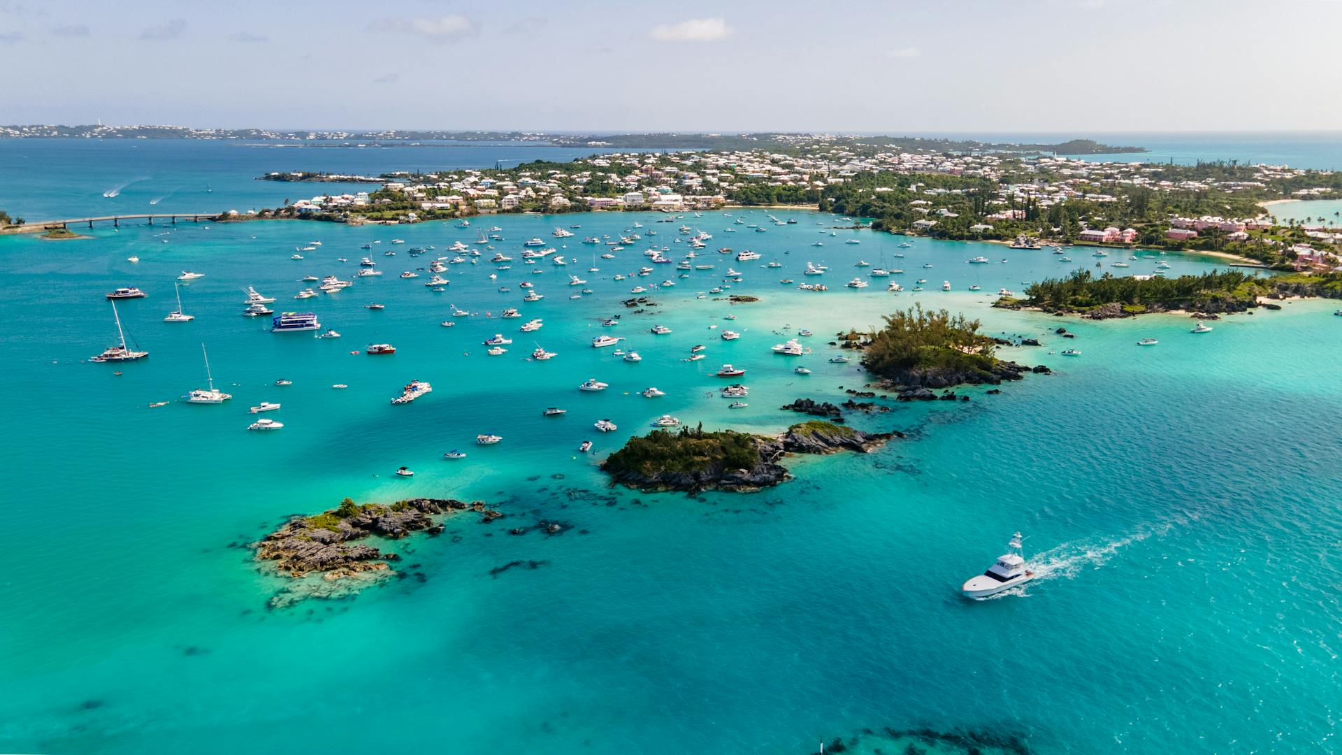 Explore the vibrant harbor of Bermuda with boats dotting the turquoise sea from above.