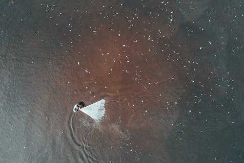 High angle of unrecognizable crop person catching fish with white net in rippling polluted by poisonous substance sea water