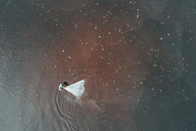 Unrecognizable Person Fishing With Net In Dirty Sea