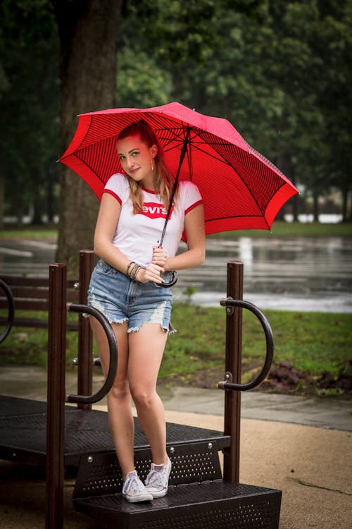 A Woman in White T-shirt and Blue Denim Shorts Holding Red Umbrella