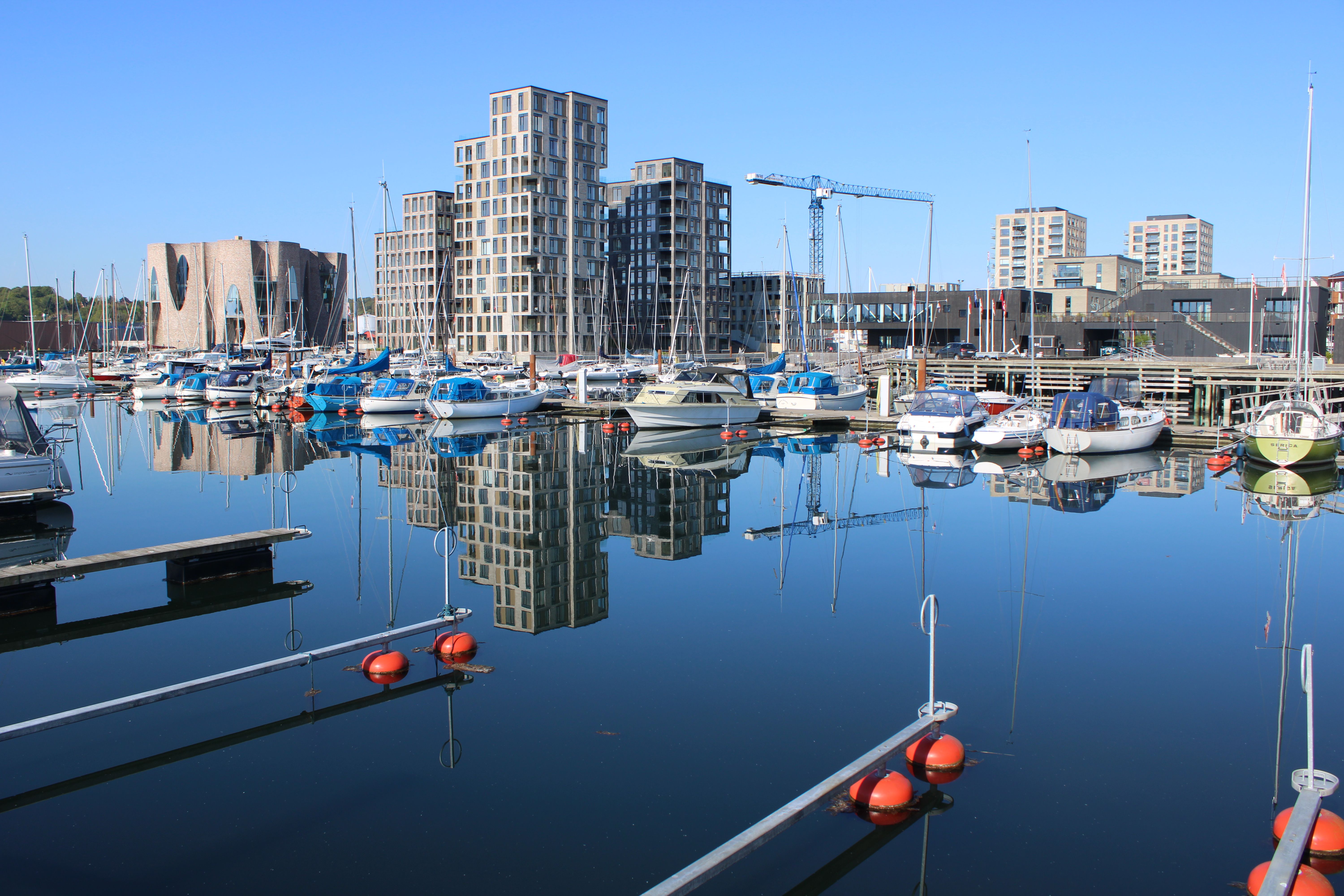 Boats moored in Vejle's harbor, reflecting modern buildings under a clear sky. — Trójmiasto