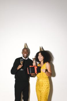 Happy couple in party hats celebrating with champagne and a gift