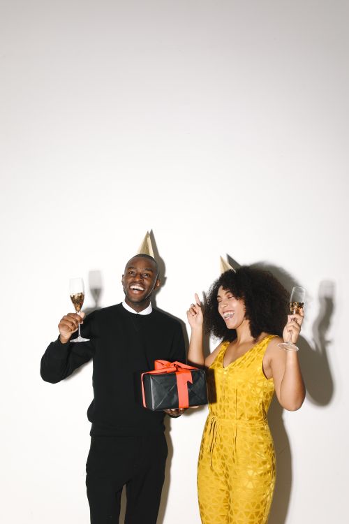 Free A happy couple wearing party hats celebrates with wine and presents, conveying festivity and joy. Stock Photo