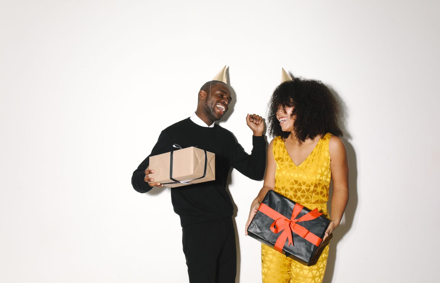 A cheerful couple wearing party hats, holding gift boxes and smiling, perfect for festive celebrations.