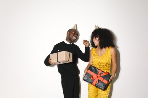 Free A cheerful couple wearing party hats, holding gift boxes and smiling, perfect for festive celebrations. Stock Photo