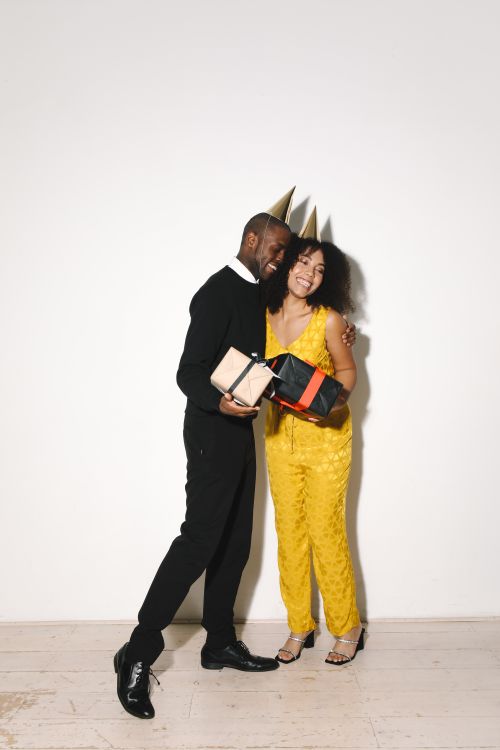 Free Smiling couple in party hats embracing and holding gifts indoors. Stock Photo
