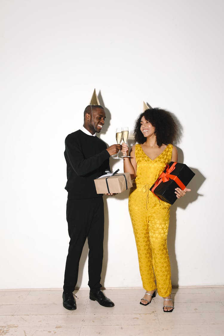 A Man And Woman Wearing Party Hat While Holding Gifts