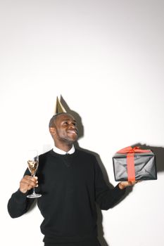 A happy man in a party hat holding a gift and champagne, celebrating indoors.
