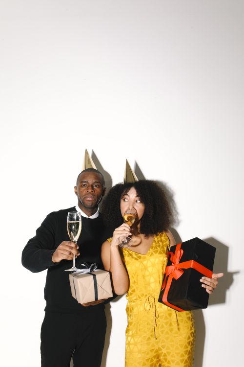 Free A joyful couple celebrates New Year with champagne and wrapped gifts, dressed in festive attire. Stock Photo