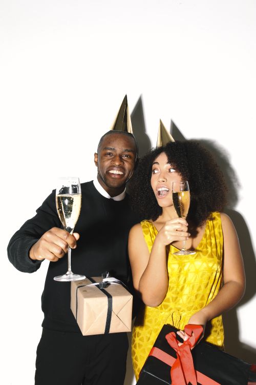 Free A happy couple toasting with champagne and wearing party hats at a festive celebration. Stock Photo