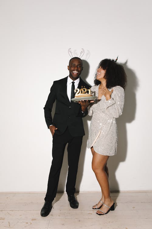 Man Holding a Cake on Plate Beside the Woman in Silver Dress