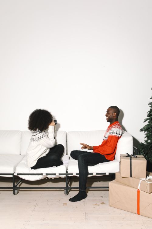 Free Two people enjoying a festive moment on a sofa, surrounded by gifts and a Christmas tree. Stock Photo