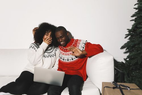Free Smiling couple in festive sweaters watching laptop on couch with holiday decor. Stock Photo