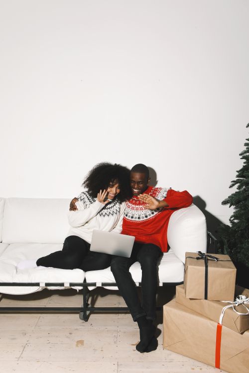 Free A joyful couple waves during a holiday video call, surrounded by gifts and festive decor. Stock Photo