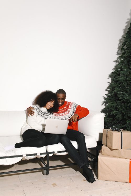 Free Couple on a couch with a laptop, enjoying holiday time next to a Christmas tree indoors. Stock Photo