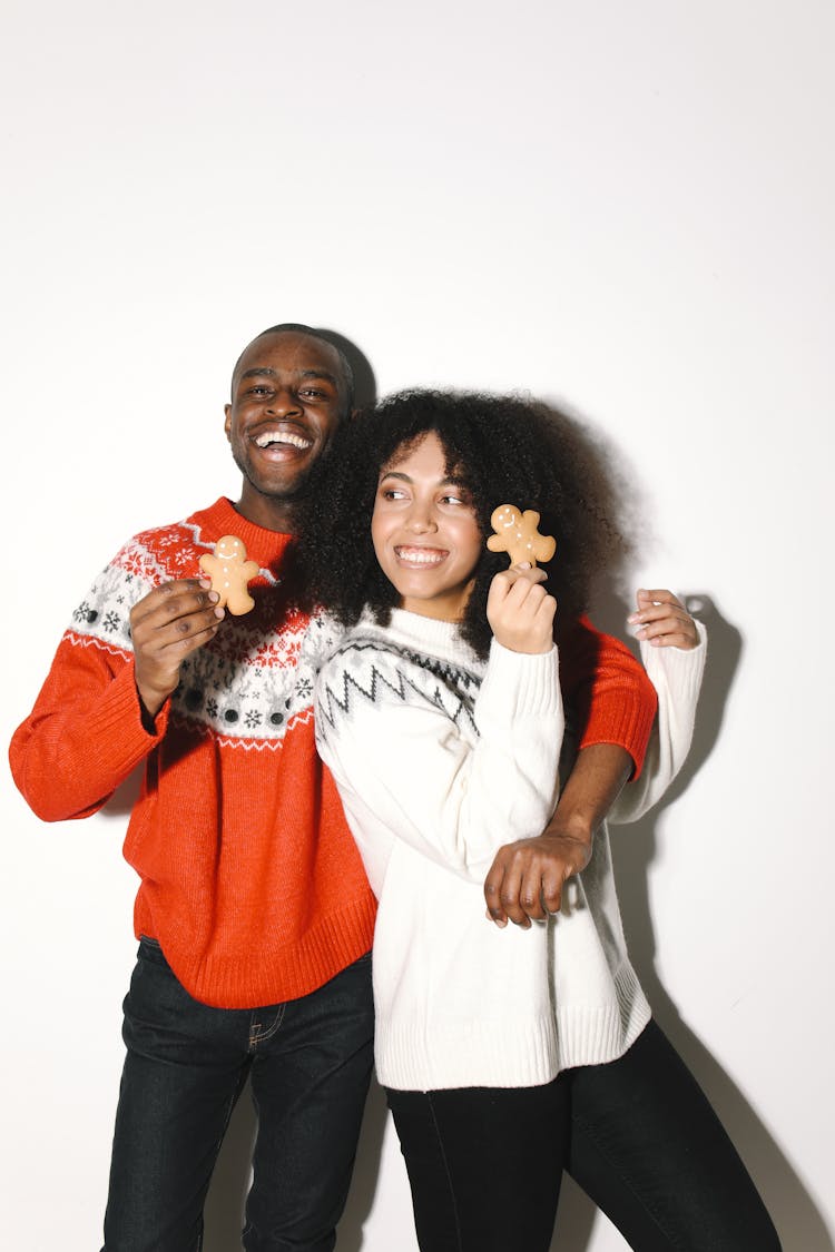 A Happy Couple Wearing Ugly Christmas Sweaters Holding Gingerbread Cookies